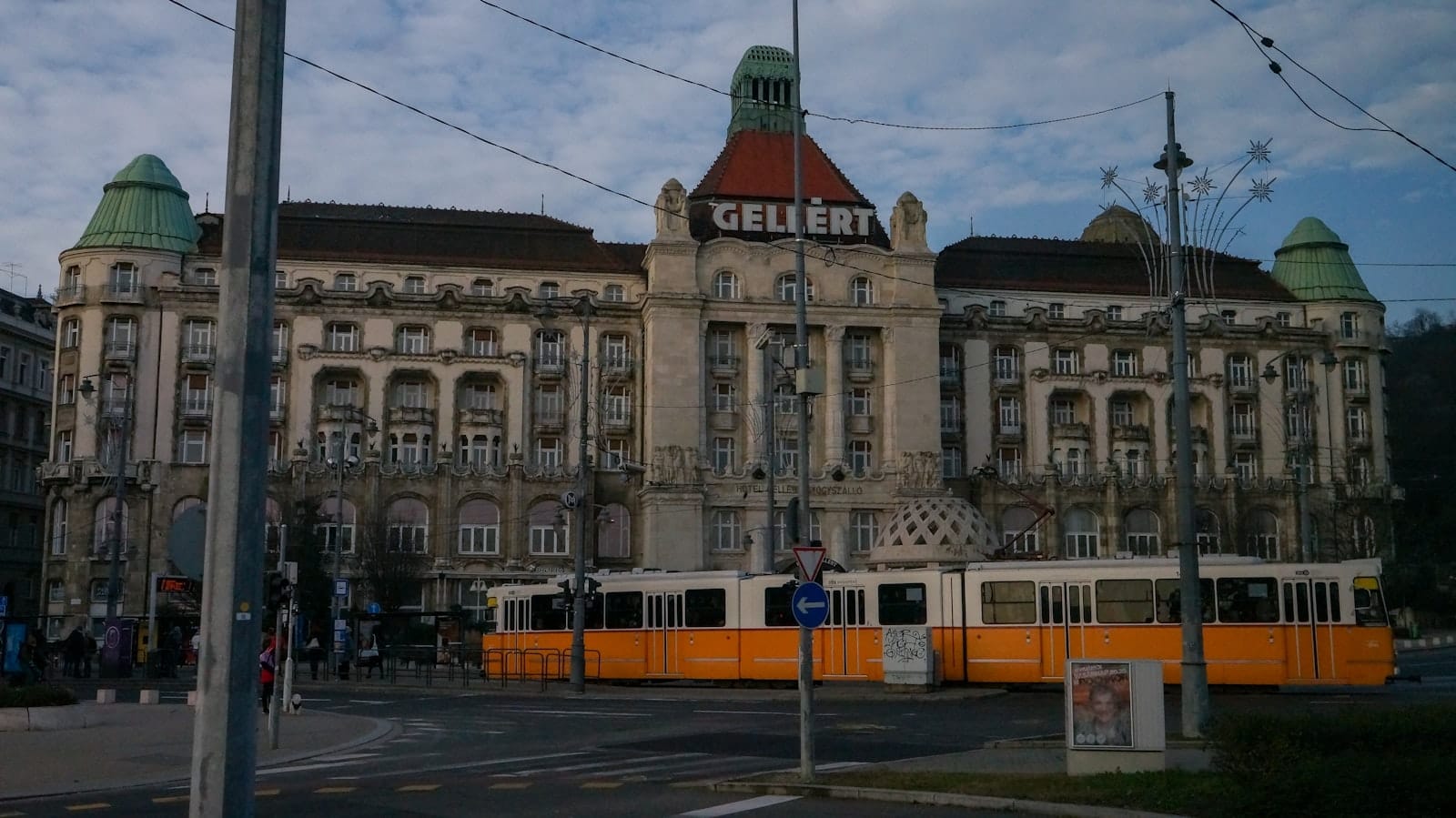Budapeşte'deki Gellért Hamamları, süslü Art Nouveau mimarisi, yeşil kubbeli kuleler ve önünden geçen sarı bir tramvayla.