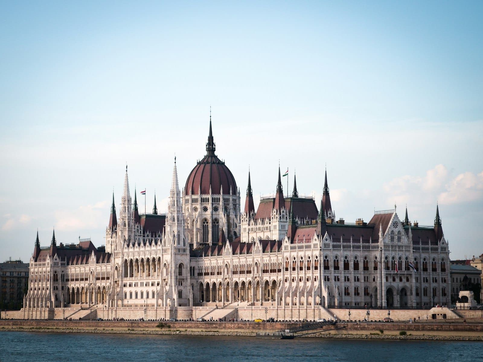 Klare Tagesansicht des Budapester Parlaments jenseits der Donau mit blauem Himmel und ruhigem Wasser.