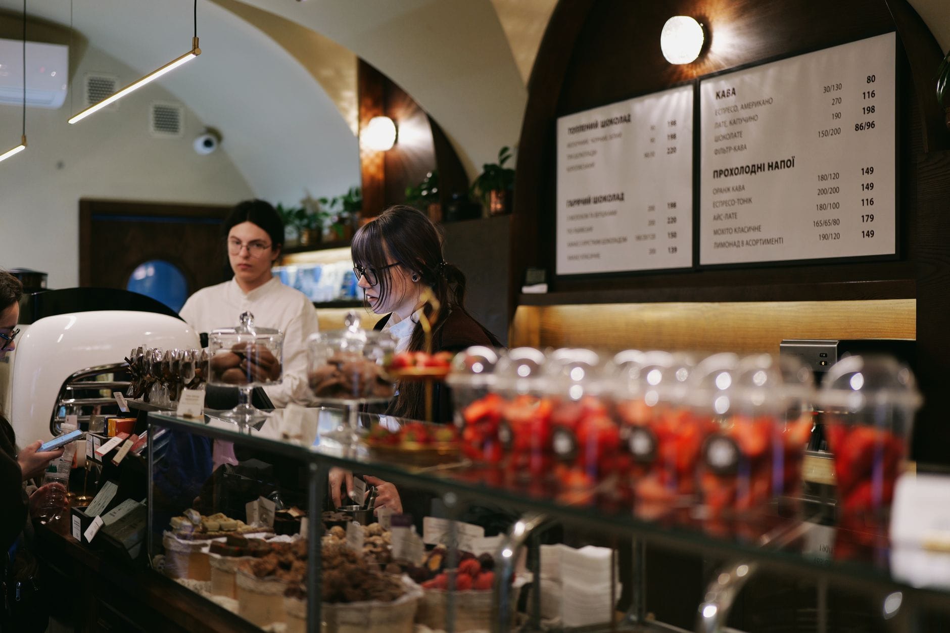 Innenraum eines klassischen europäischen Cafés in Budapest mit Personal hinter einer Theke, die Gebäck, Schokolade und frische Fruchtdesserts präsentiert.