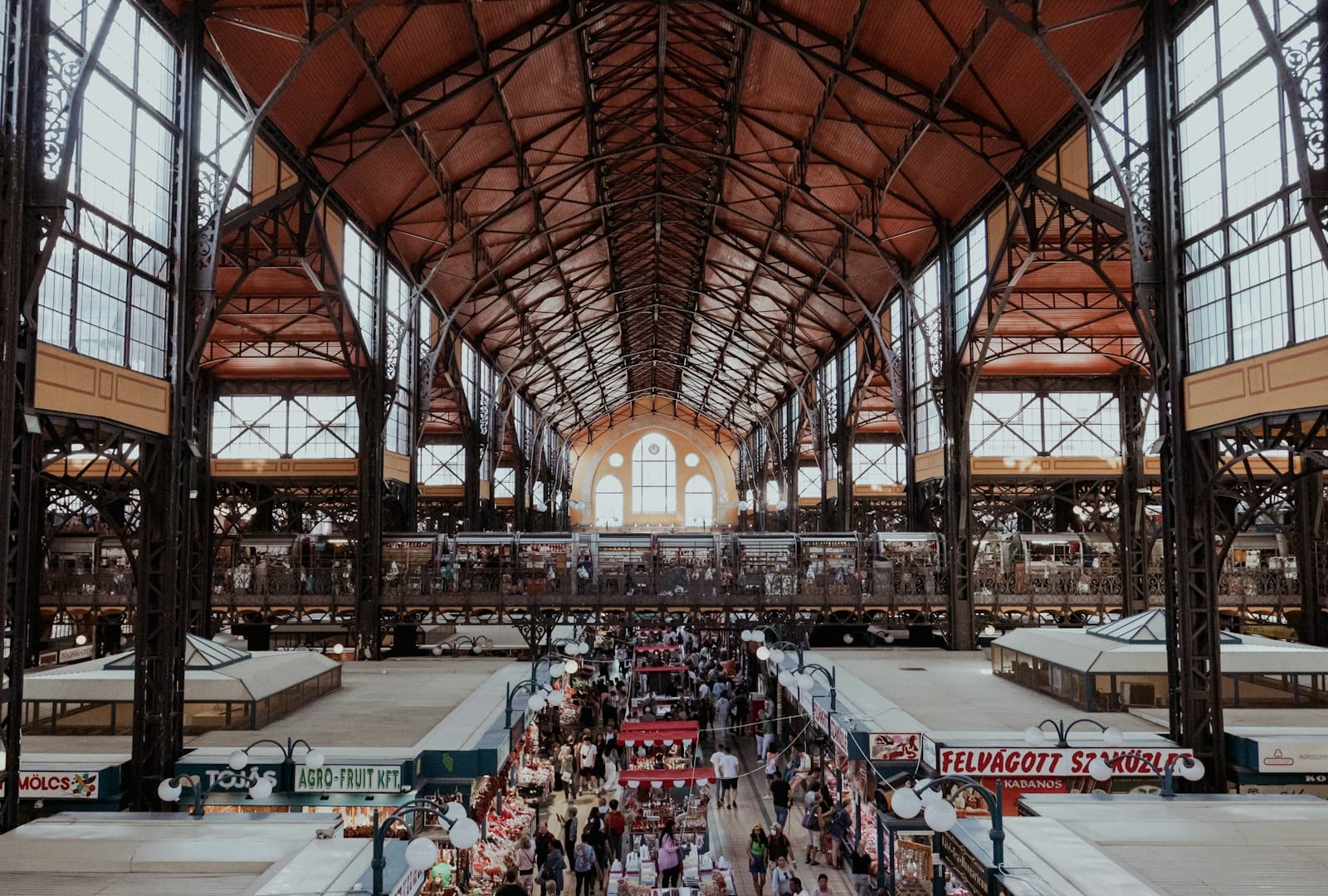 Weitwinkelansicht des Innenraums der Zentralmarkthalle Budapest mit belebten Ständen, Einkäufern und Eisenarchitektur unter einem hohen Gewölbedach.