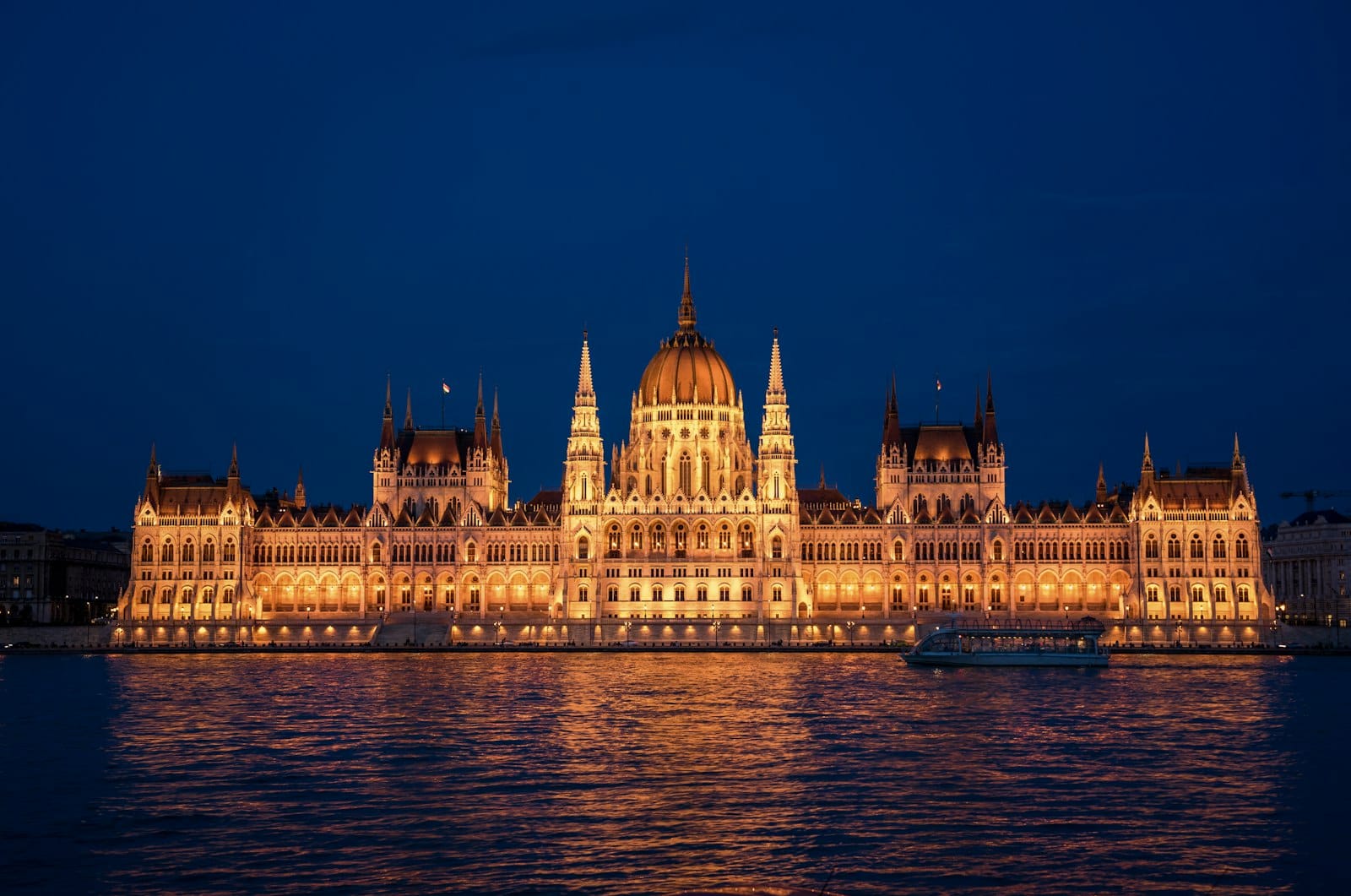 Das ungarische Parlamentsgebäude in Budapest bei Nacht wunderschön beleuchtet, im Fluss Donau gespiegelt unter einem tiefdunkelblauen Himmel – ein Bild voller Eleganz und Grandeur.