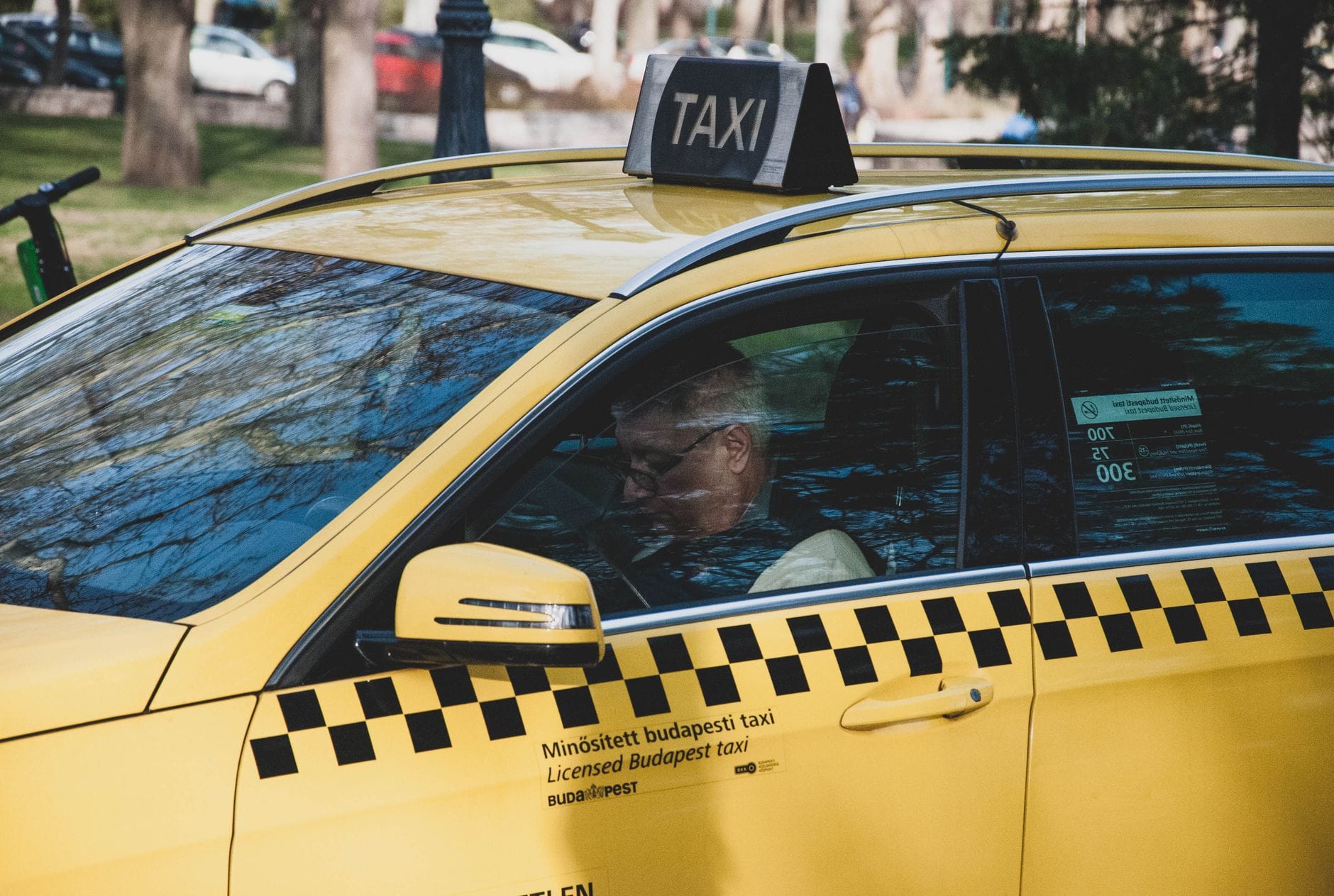 Ein gelbes Budapester Taxi parkt an einem Park, der Fahrer sitzt darin – ein klassisches Beispiel für eine der häufigsten Touristenfallen der Stadt.