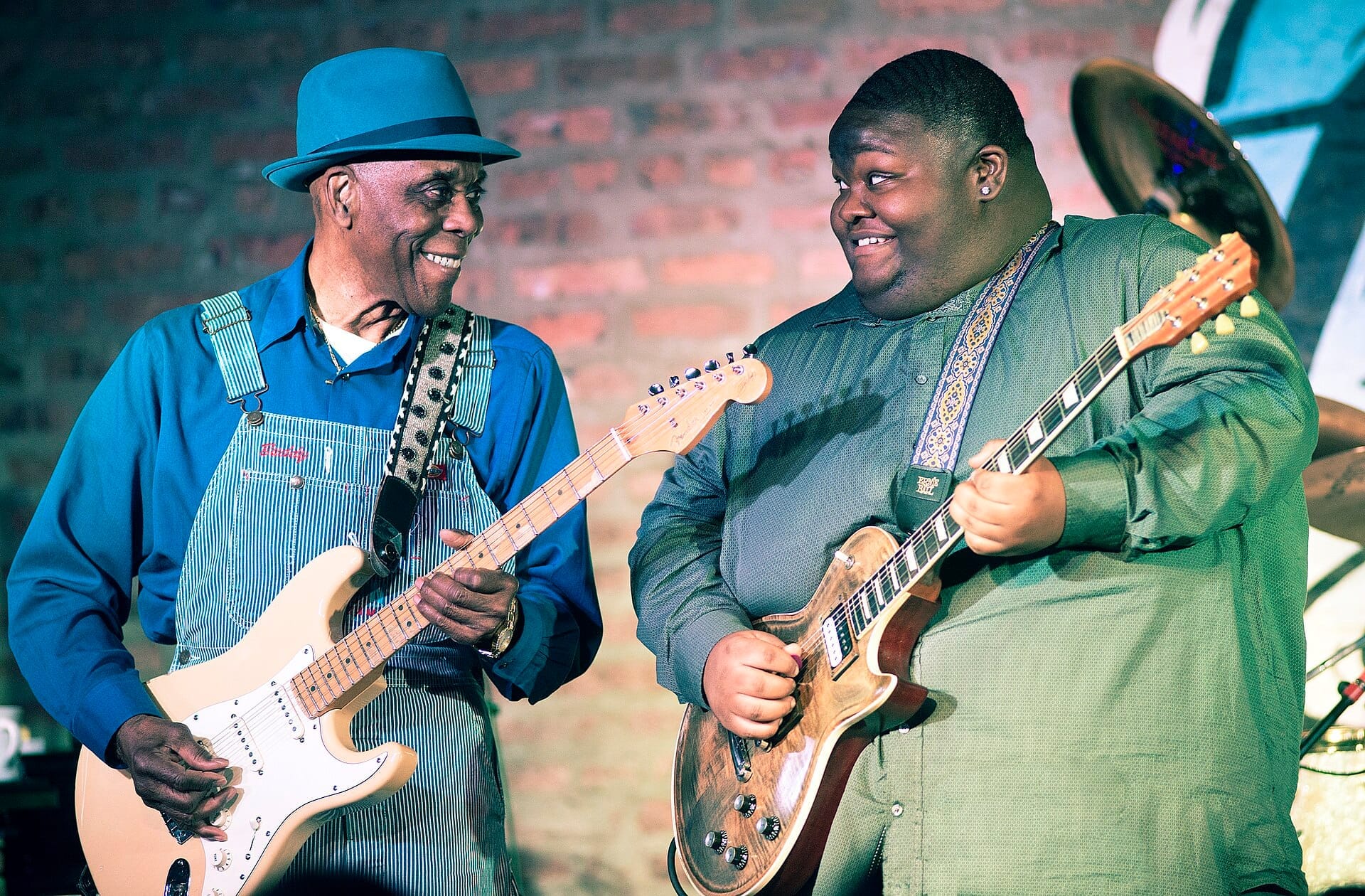 Due musicisti suonano chitarre elettriche sul palco del Buddy Guy's Legends, con un muro di mattoni come sfondo e luci del palco intense.