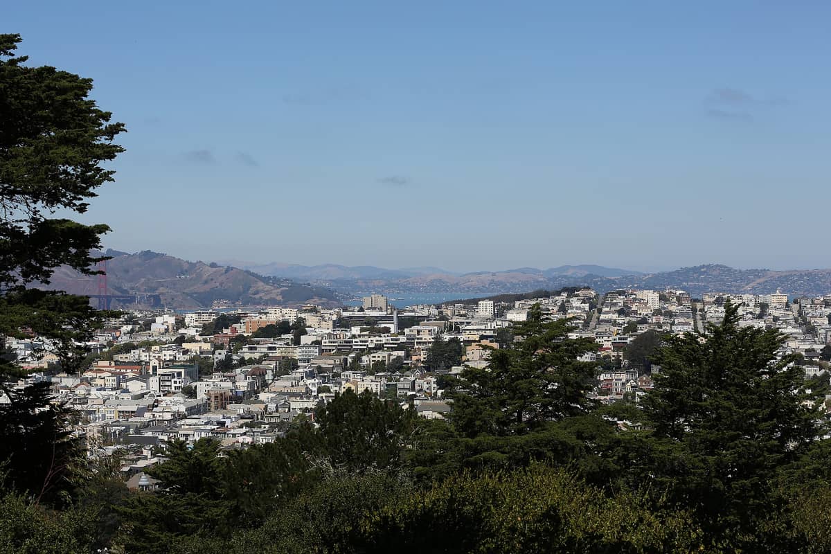 Vista panorámica desde Buena Vista Park con los barrios de San Francisco, árboles en primer plano, colinas al fondo y el puente Golden Gate visible a lo lejos.