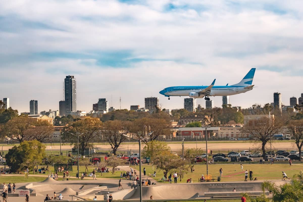 เครื่องบินพาณิชย์กำลังแลนดิ้งที่สนามบิน Aeroparque Jorge Newbery ท่ามกลางวิวเมืองบัวโนสไอเรสและสวนในช่วงกลางวันสดใส