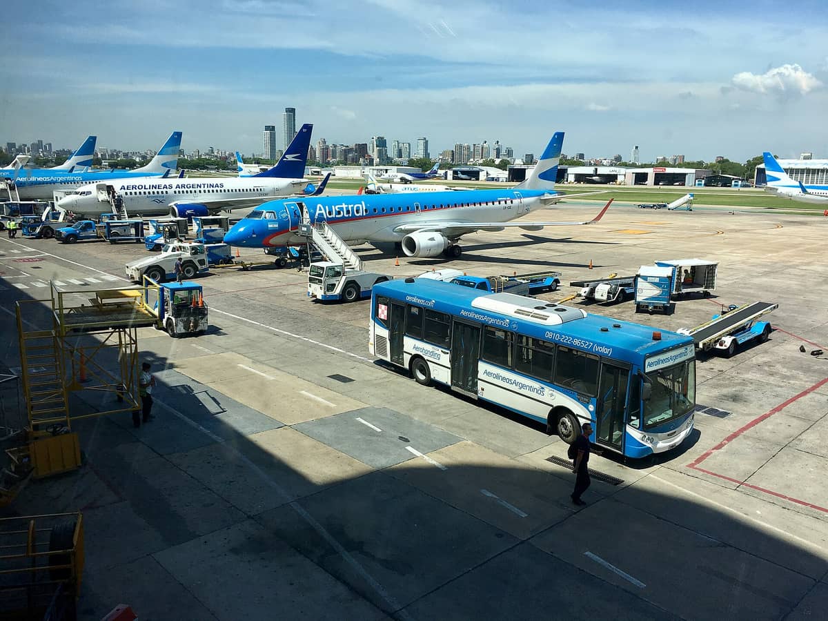 มุมมองจากพื้นดินของสนามบิน Aeroparque ในบัวโนสไอเรส แสดงให้เห็นเครื่องบินบนลานจอด เส้นขอบฟ้าของเมือง และรถรับส่งของสนามบิน