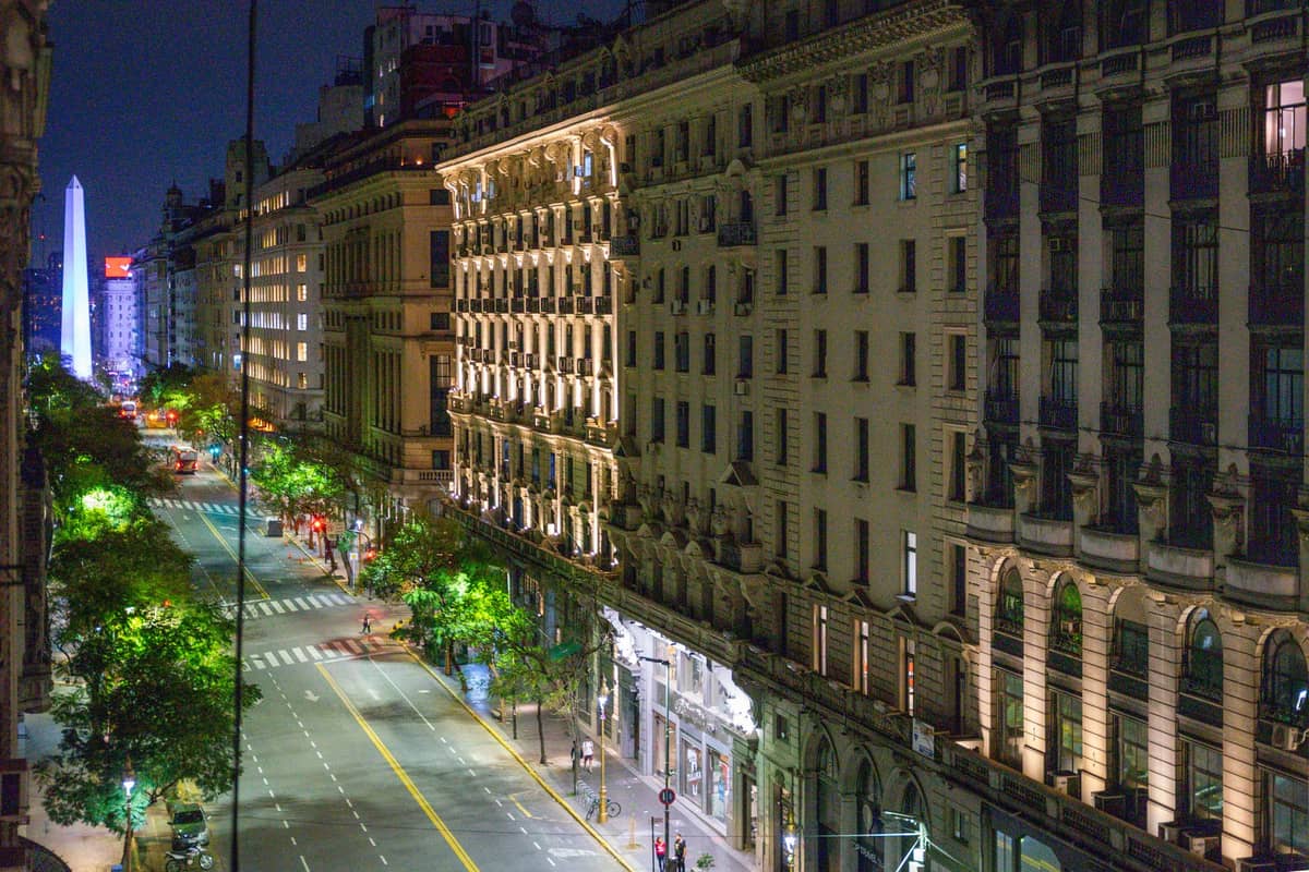 วิวยามค่ำคืนของ Avenida 9 de Julio พร้อมอาคารประวัติศาสตร์และ Obelisco ในระยะไกล ใกล้กับ Microcentro บัวโนสไอเรส ซึ่งเป็นที่ตั้งของสำนักงานแลกเปลี่ยนเงินตรา