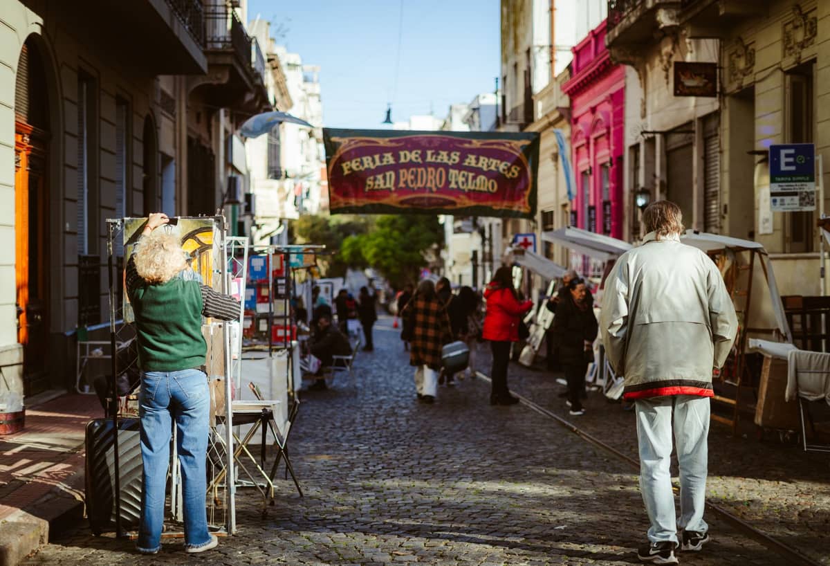 ถนนหินกรวดในย่าน San Telmo ของ Buenos Aires พร้อมแผงตลาดริมถนน อาคารสีสันสดใส และป้าย Feria de San Pedro Telmo