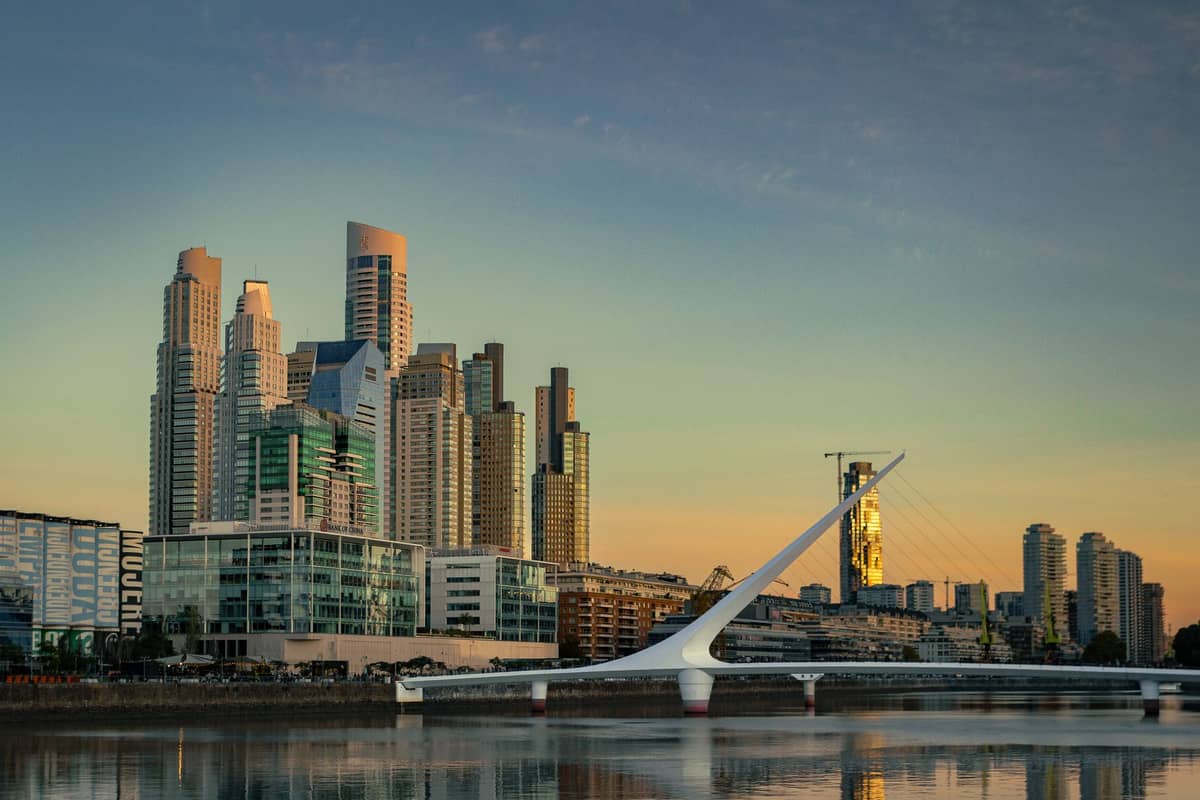 ตึกระฟ้ากระจกสมัยใหม่และสะพานคนเดิน Puente de la Mujer อันโดดเด่นเหนือน้ำริมฝั่ง Puerto Madero ยามพระอาทิตย์ตกดินในบัวโนสไอเรส