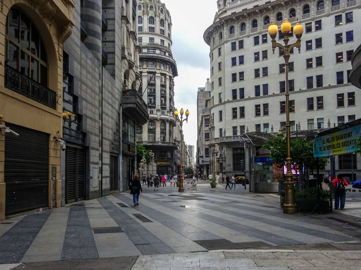ถนนคนเดินกว้างในใจกลาง Buenos Aires พร้อมอาคารประวัติศาสตร์สไตล์ยุโรป โคมไฟประดับตกแต่ง และผู้คนเดินเล่นในวันที่มีเมฆมาก