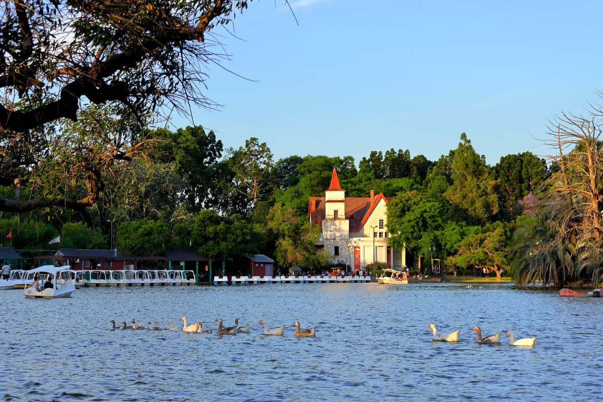 ทะเลสาบ Palermo ในบัวโนสไอเรส มีเรือสีสันสวย เรือถีบ และเป็ดในน้ำ กับอาคารหลังคาแดงสไตล์เทพนิยายเป็นฉากหลัง ท่ามกลางสวนเขียวชอุ่ม
