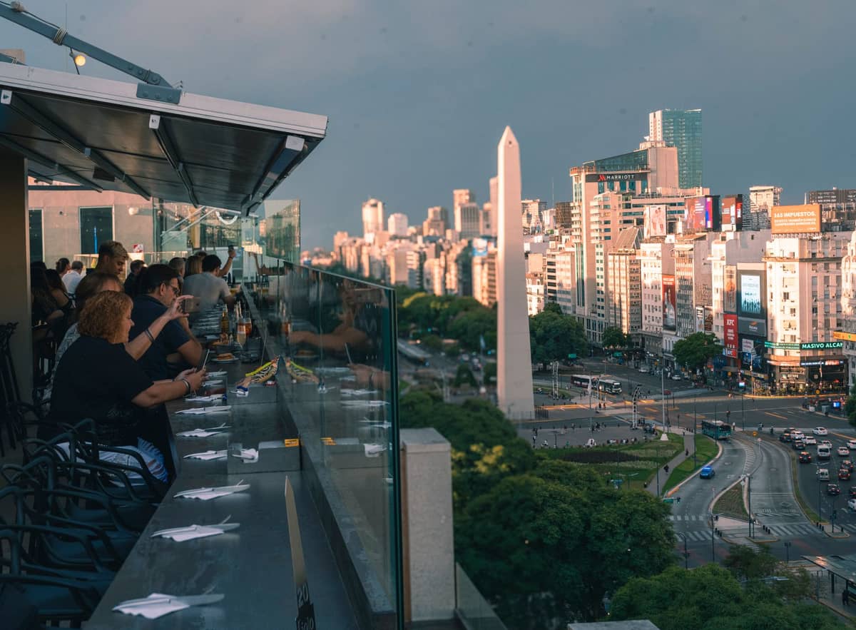 ภาพมุมสูงบนถนน Avenida 9 de Julio ของบัวโนสไอเรส เห็นโอเบลิสก์และตึกระฟ้าในแสงยามเย็นจากร้านอาหารบนดาดฟ้า