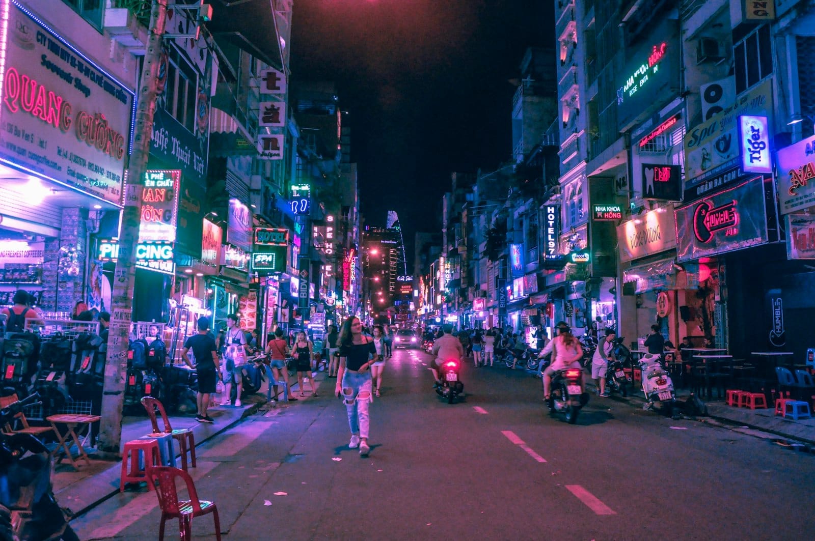 Bui Vien Walking Street de noche, llena de bares con luces de neón, tiendas, peatones y motocicletas bajo los coloridos y brillantes letreros de la ciudad.