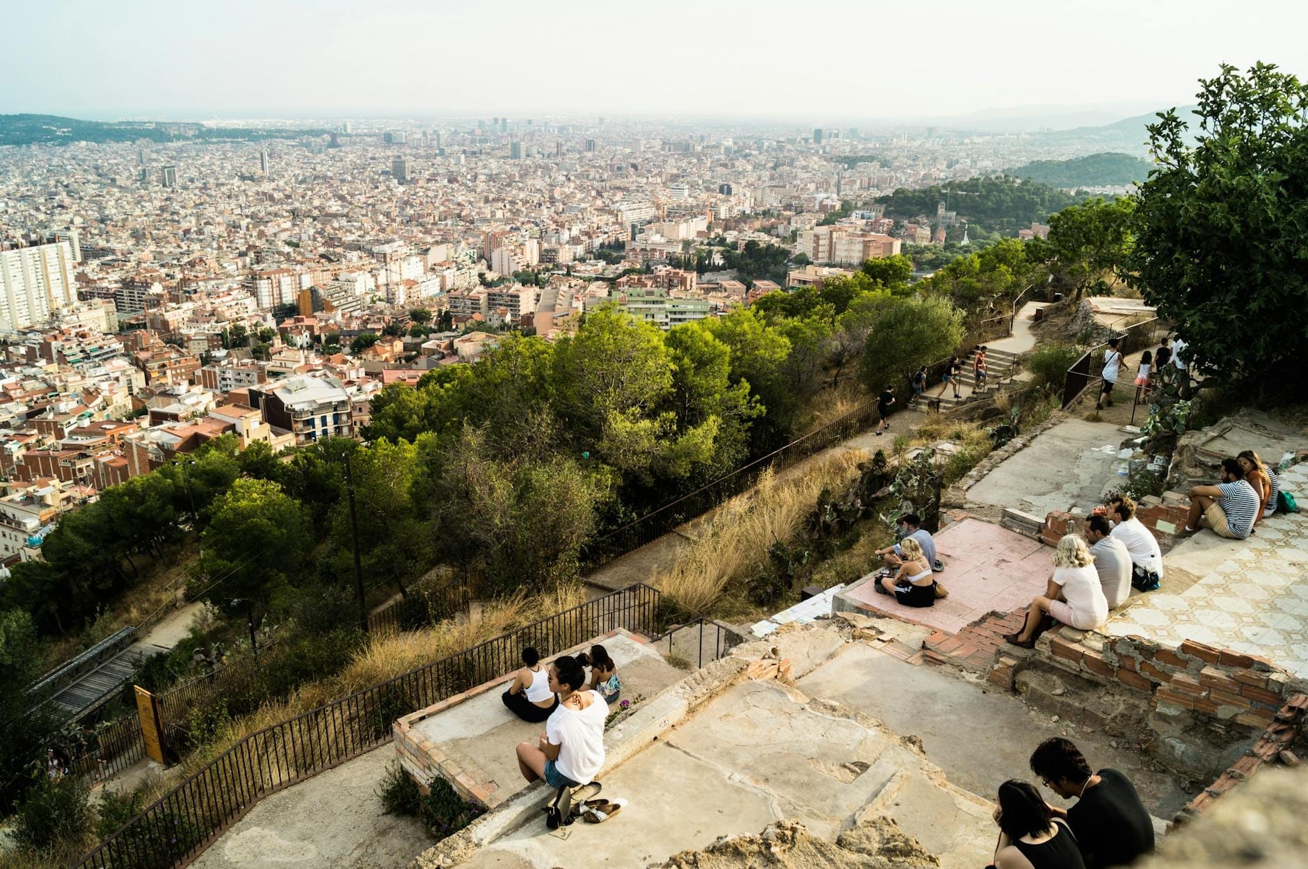 People relaxing on the historic Bunkers del Carmel ruins with panoramic views over Barcelona city, featuring the sea and famous landmarks in the distance.