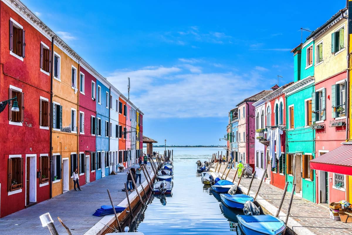 ภาพคลองสีสันสดใสบนเกาะบูราโน บ้านทาสีแดง เหลือง เขียว น้ำเงินเรือจอดริมคลอง ใต้ท้องฟ้าสดใส