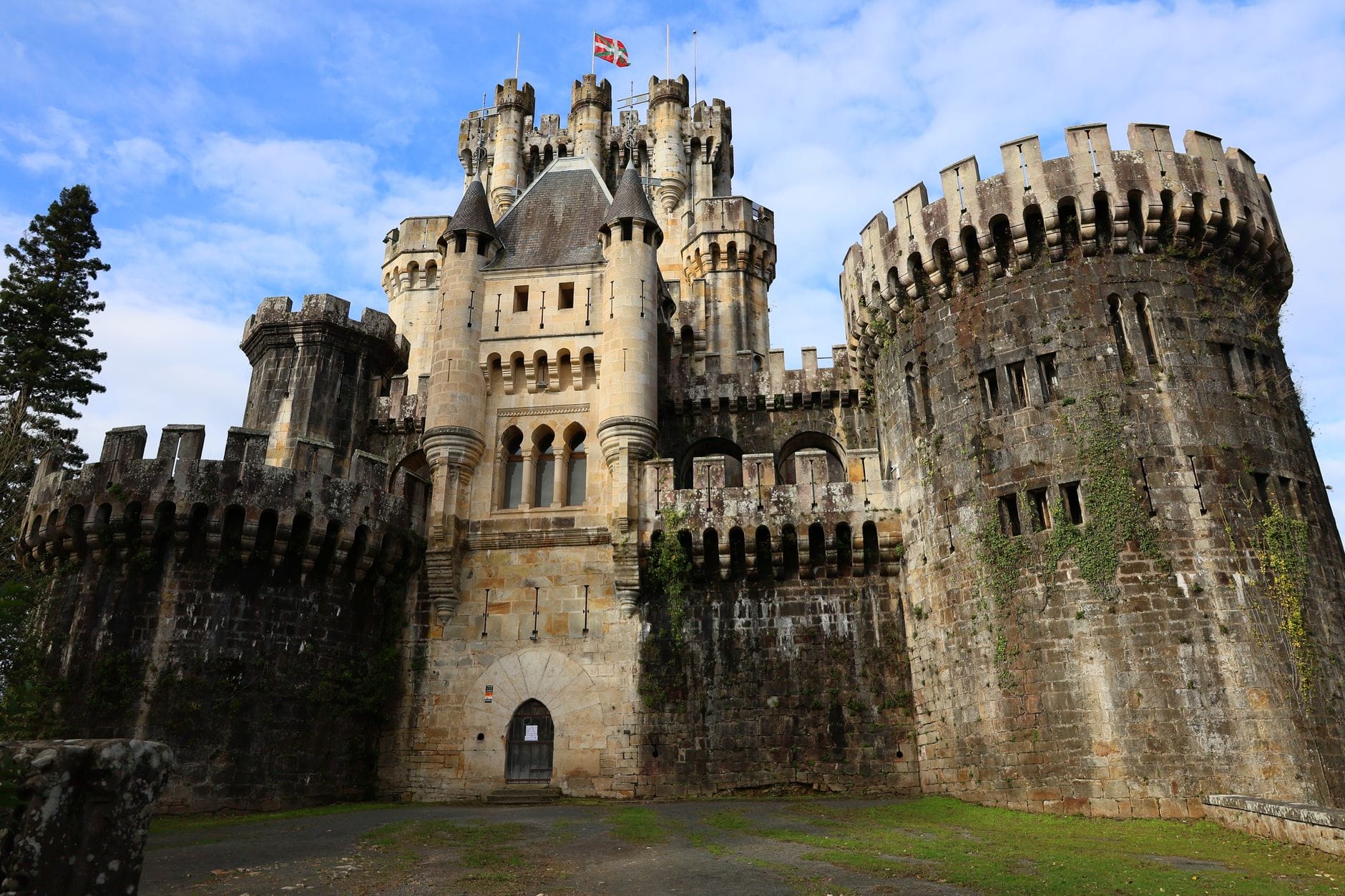 Dramatic neo-Gothic Butrón Castle with round turrets and central tower, framed by blue sky and lush greenery, showcasing its imposing exterior in the Basque Country.