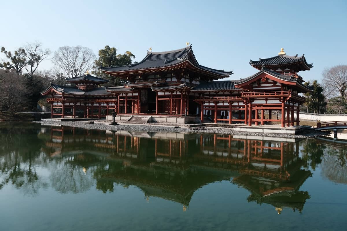 Wide view of Byodo-in Temple's Phoenix Hall reflected in the pond on a clear day, showcasing its iconic architecture and tranquil surroundings.