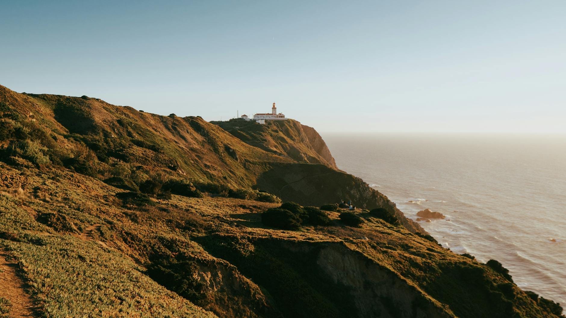 Vista panoramica delle imponenti scogliere di Cabo da Roca che si elevano sull'Oceano Atlantico, con il faro arroccato sul bordo sotto un cielo sereno.