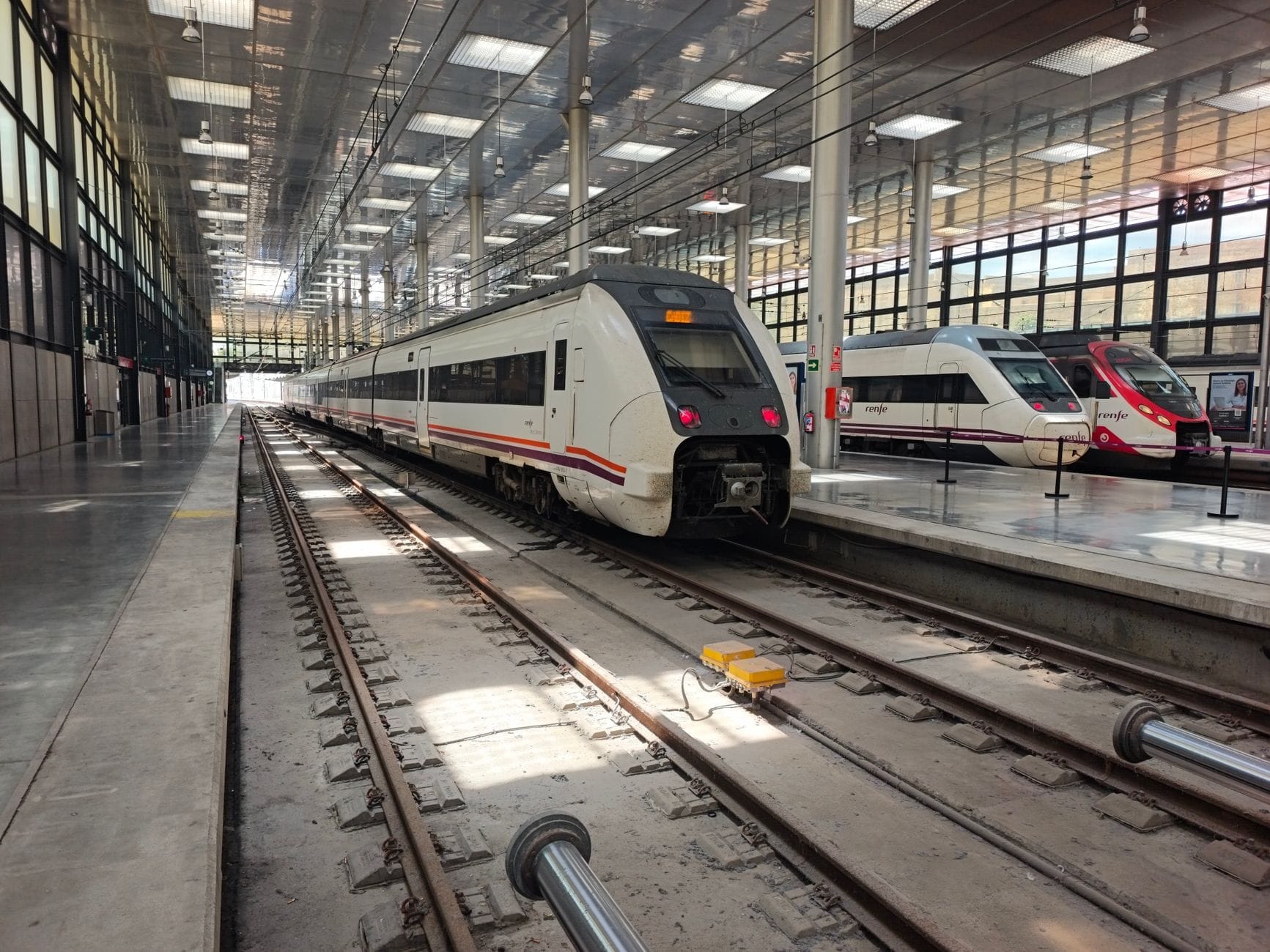 Tren moderno en un andén de estación con techo de cristal luminoso, que ilustra las opciones de viaje en tren para llegar a Cádiz, España.