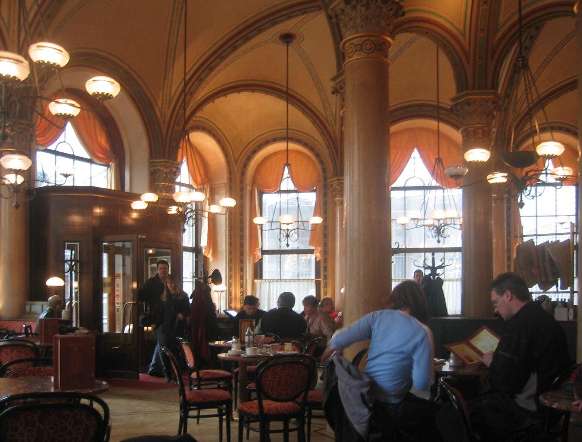 Innenansicht des Café Central Wien mit verzierten Säulen, Bogenfenstern und Gästen, die bei warmem Kronleuchter-Licht Kaffee genießen.