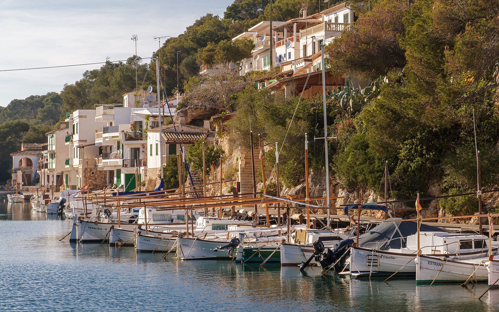 Tradizionali barche da pesca ormeggiate lungo le acque calme di Cala Figuera, con case imbiancate a calce e rigogliosa vegetazione che sale lungo il versante collinare