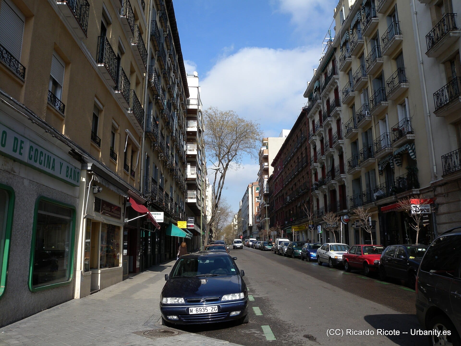 Vista della strada Calle de Ponzano a Madrid, fiancheggiata da alti condomini, auto parcheggiate e insegne di negozi in una giornata di sole.