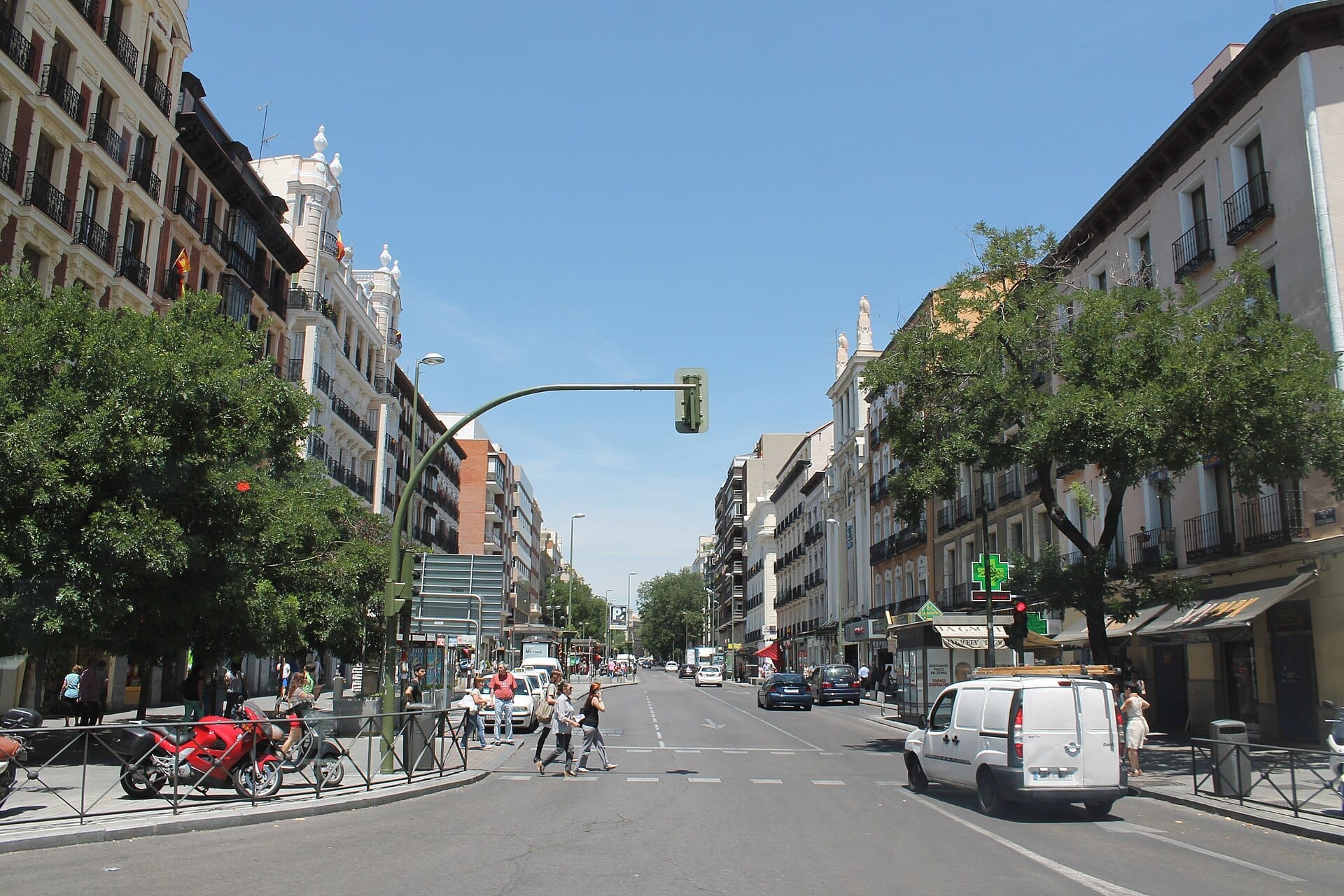 Vista della Calle de Fuencarral a Madrid con edifici storici, traffico stradale, alberi e pedoni in una giornata di sole.