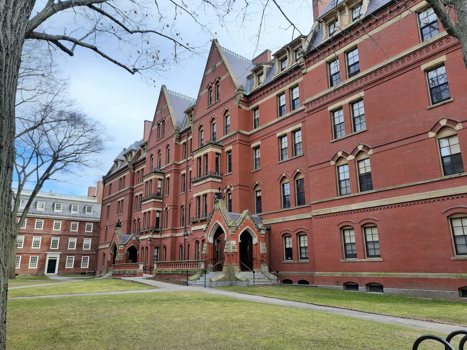 อาคารอิฐแดงใน Harvard Yard ท่ามกลางวันที่อากาศแจ่มใส สนามหญ้าสีเขียวกับทางเดิน บรรยากาศ Ivy League ที่โดดเด่นของ Cambridge