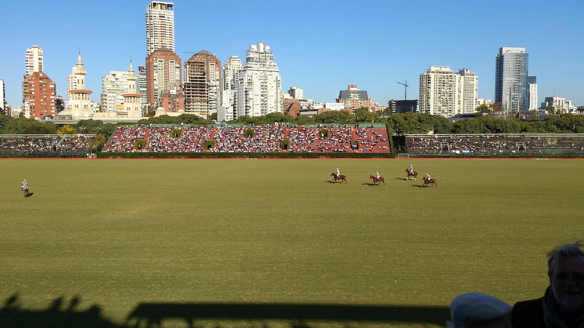 มุมกว้างของ Campo Argentino de Polo ขณะจัดงาน แข่งโปโลและผู้ชมเต็มอัฒจันทร์ โดยมีเส้นขอบฟ้าของบัวโนสไอเรสเป็นฉากหลัง