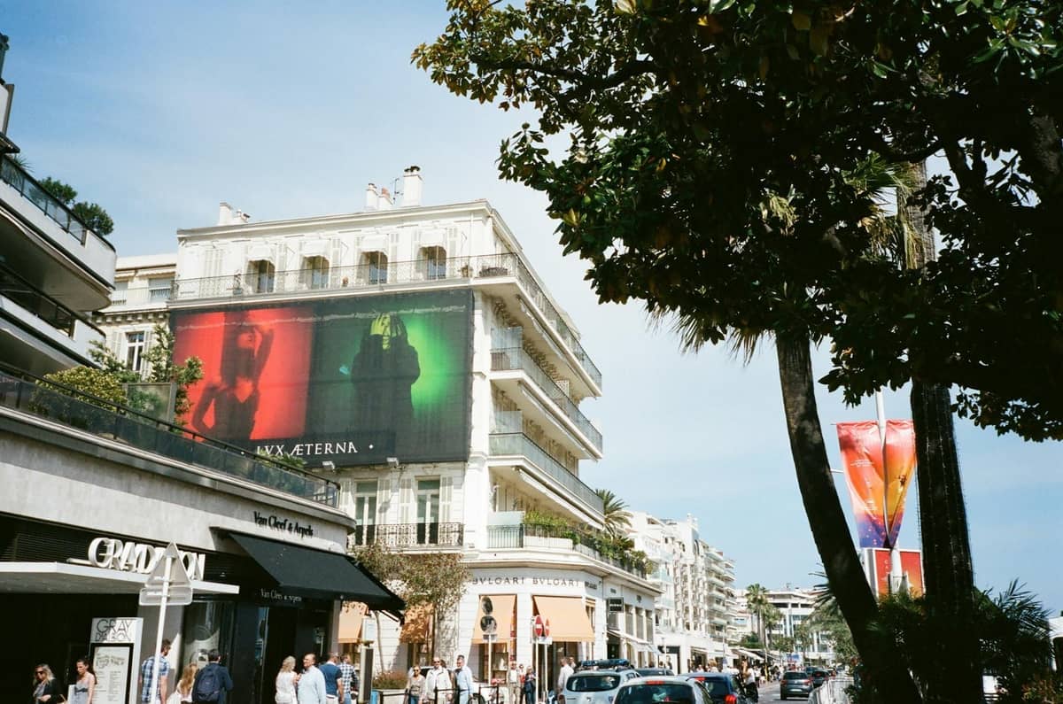 Concurrida calle de Cannes flanqueada por boutiques de lujo, palmeras, elegantes edificios y personas de compras en un día soleado.
