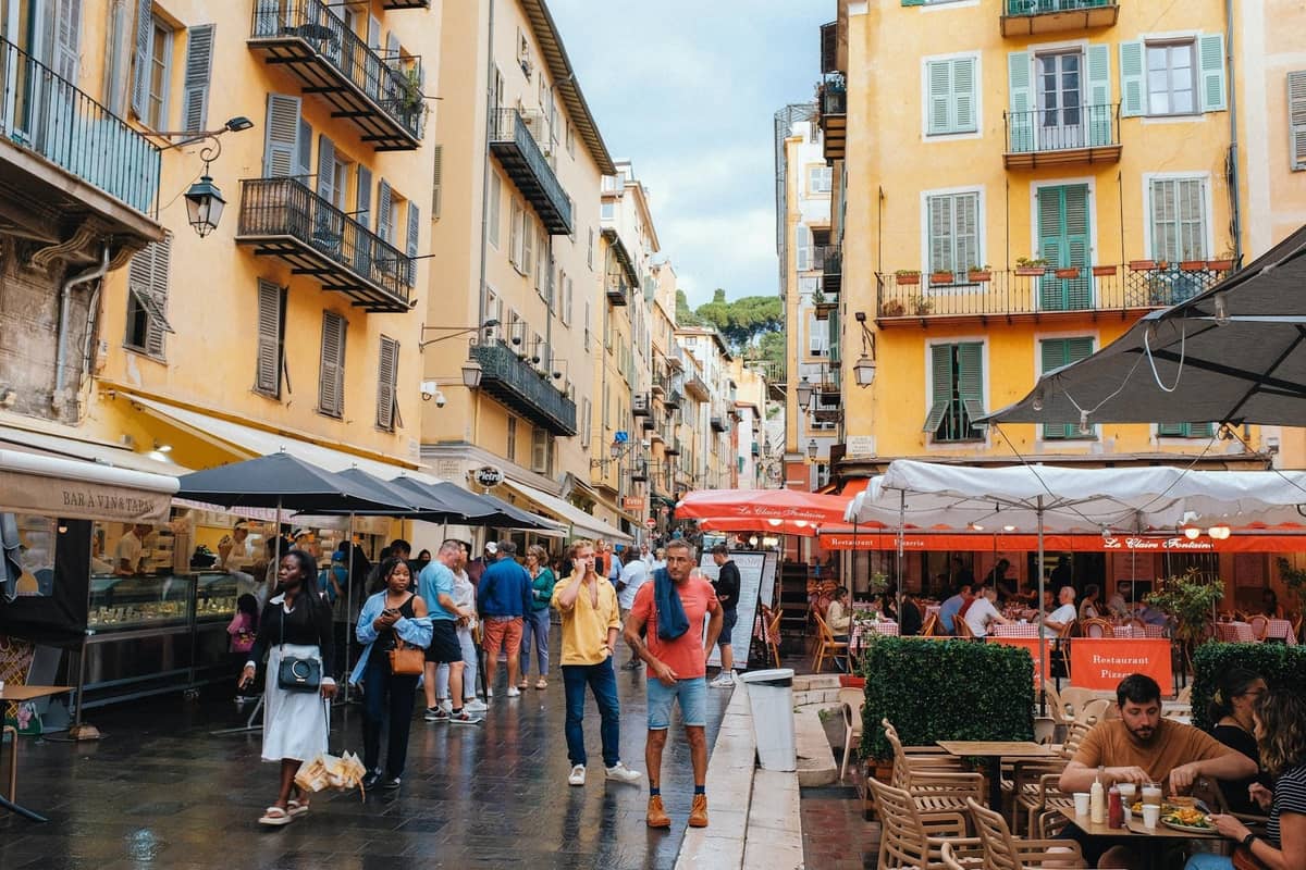 Calle peatonal en el casco antiguo de Cannes, Le Suquet, con edificios amarillos, tiendas, cafés al aire libre y gente de compras y comiendo.