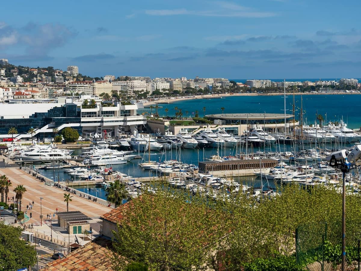 Açık bir gökyüzü altında yatlar, modern binalar ve mavi Akdeniz ile Cannes limanının panoramik görünümü.
