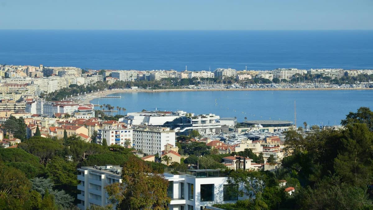 Weitläufige Erhöhte Aussicht auf Cannes mit der Kurstadt, der Bucht, den Stränden und dem Mittelmeer unter klarem blauem Himmel.