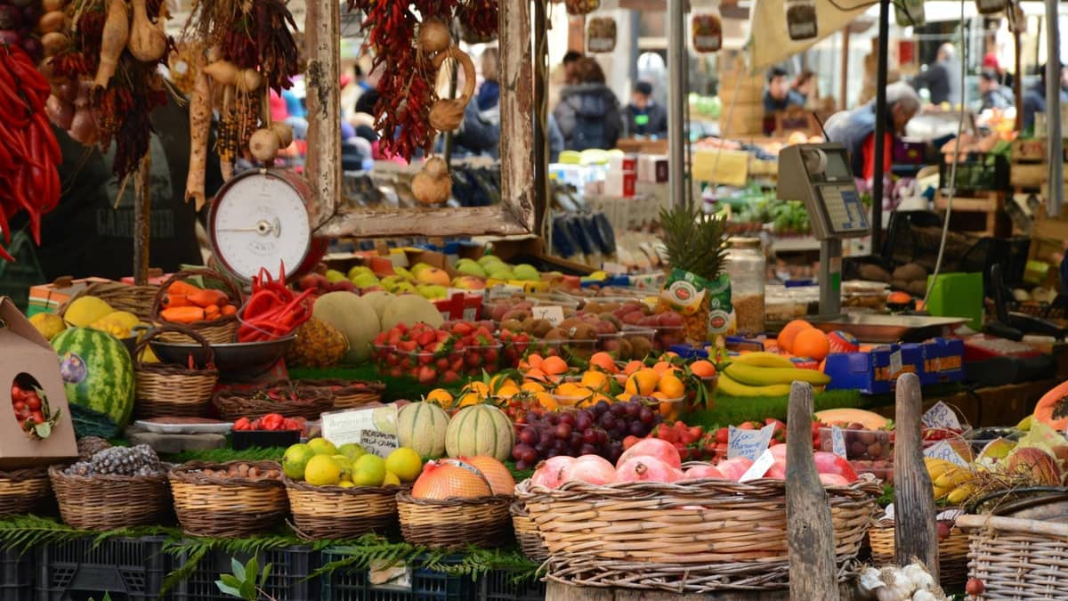 Obfite kosze kolorowych świeżych produktów wystawione na tętniącym życiem targu na świeżym powietrzu, z kupującymi w tle.
