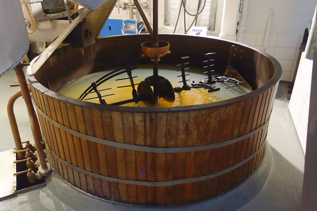 Um grande tanque de madeira com equipamentos de mistura em metal na Cervejaria Cantillon, mostrando a área tradicional de produção de cerveja lambic dentro do histórico espaço em Bruxelas.