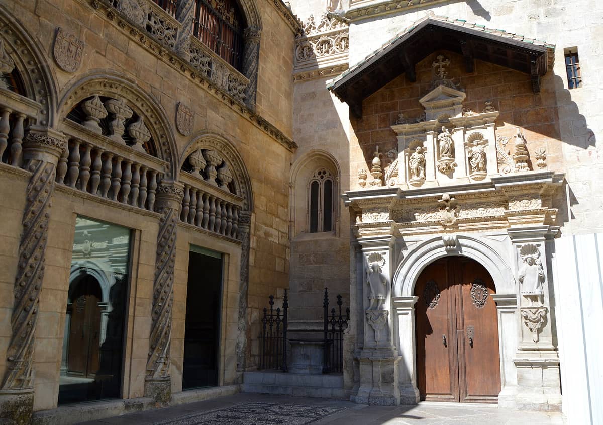 ทางเข้าและหน้าจั่วของ Capilla Real de Granada แสดงงานหินแกะสลักประณีต รูปปั้น และซุ้มประตูใต้แสงแดดจ้า