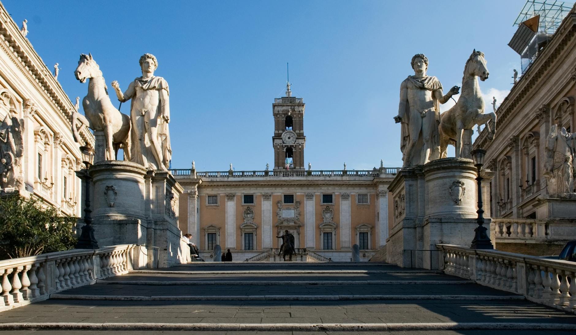 The grand staircase and statues leading up to Piazza del Campidoglio on Capitoline Hill, with Michelangelo's palazzo and bright blue sky in the background.