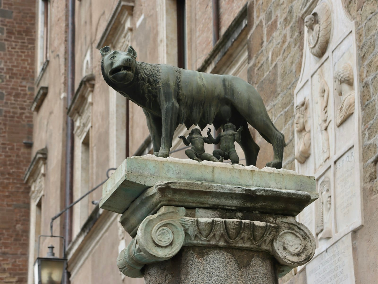 Bronze statue of the she-wolf nursing Romulus and Remus, displayed outside Capitoline Museums against historic stone walls in Rome.