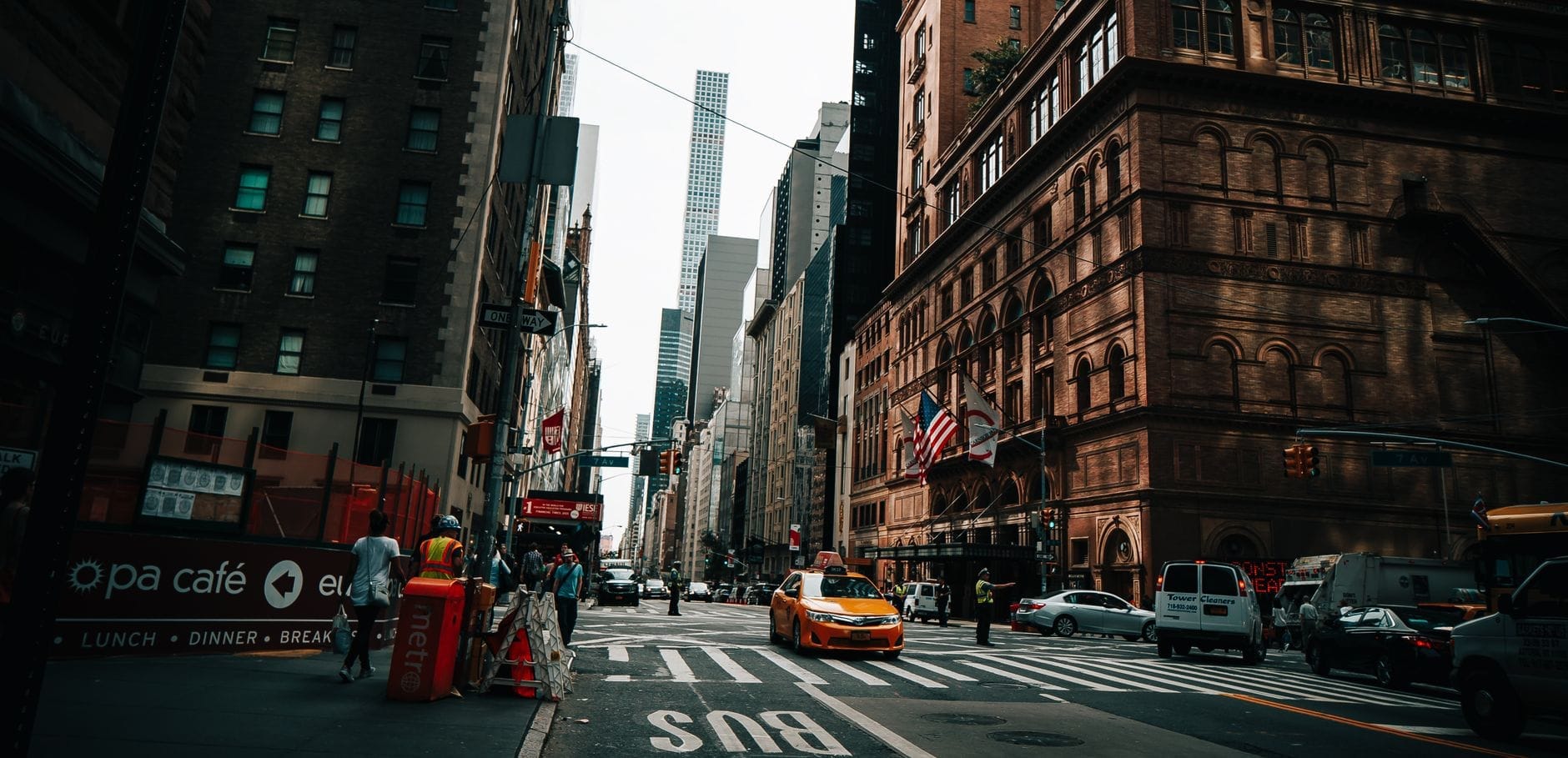 Vista dalla strada della caratteristica facciata in mattoni della Carnegie Hall a Midtown Manhattan in una giornata animata, con taxi gialli, pedoni e grattacieli sullo sfondo.