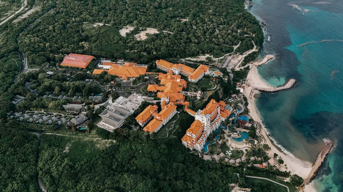 Aerial view of Decameron Barú resort with orange-roofed buildings, surrounded by lush greenery and adjacent to white sandy beach and turquoise sea.