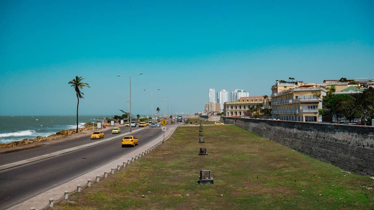 Landscape view of Cartagena's historic defensive walls running parallel to the Caribbean Sea, with cannons visible and taxis driving along the waterfront road.