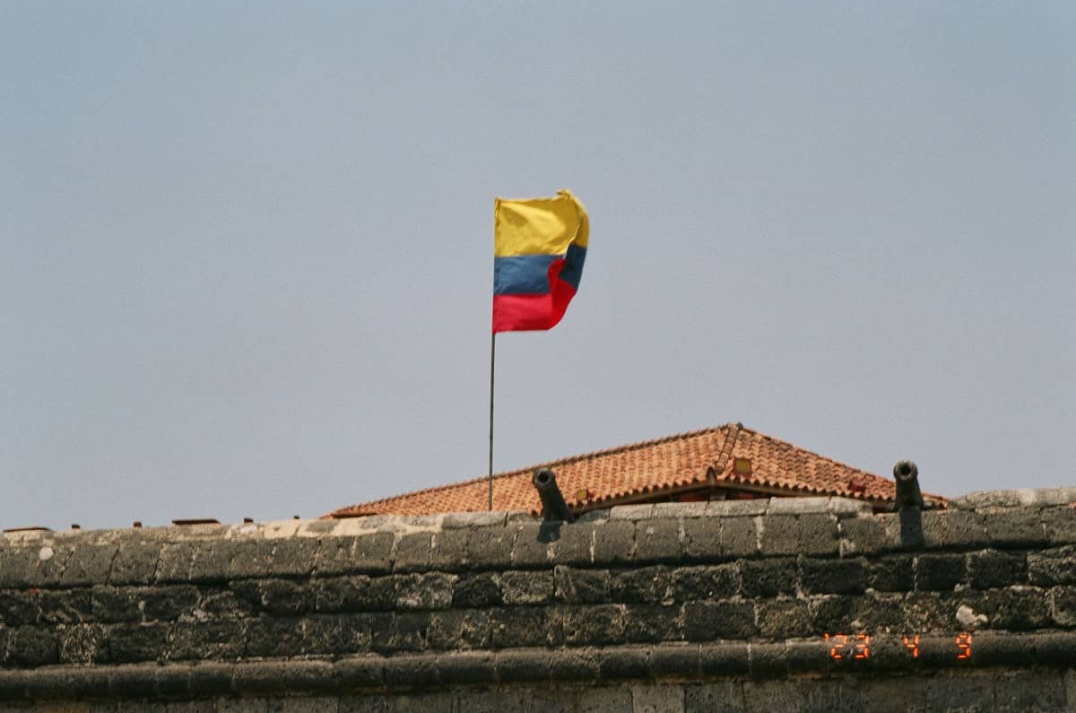 Stone defensive wall with cannons and Colombian flag, typical of Cartagena's historic city walls, under a clear sky.