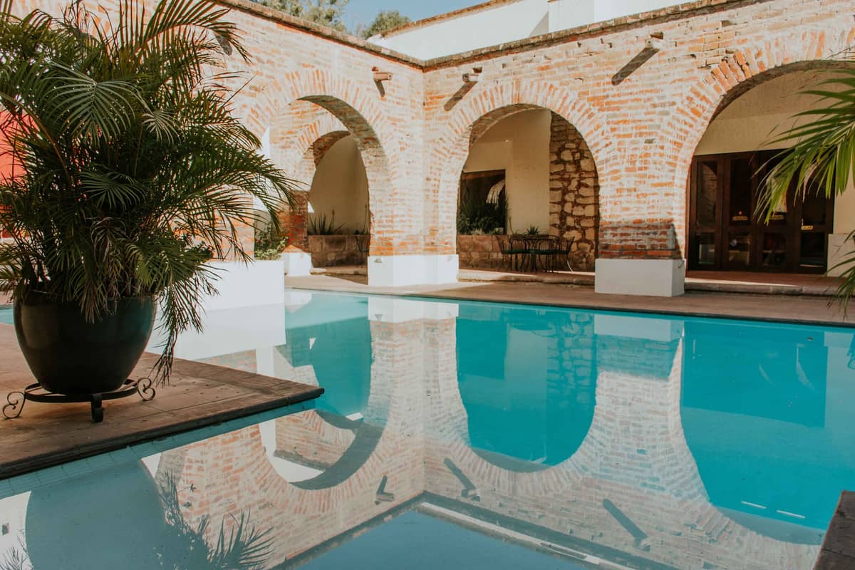 Boutique-style courtyard with arched brick walls, a turquoise pool, tropical plants, and a romantic ambiance in a restored colonial mansion.
