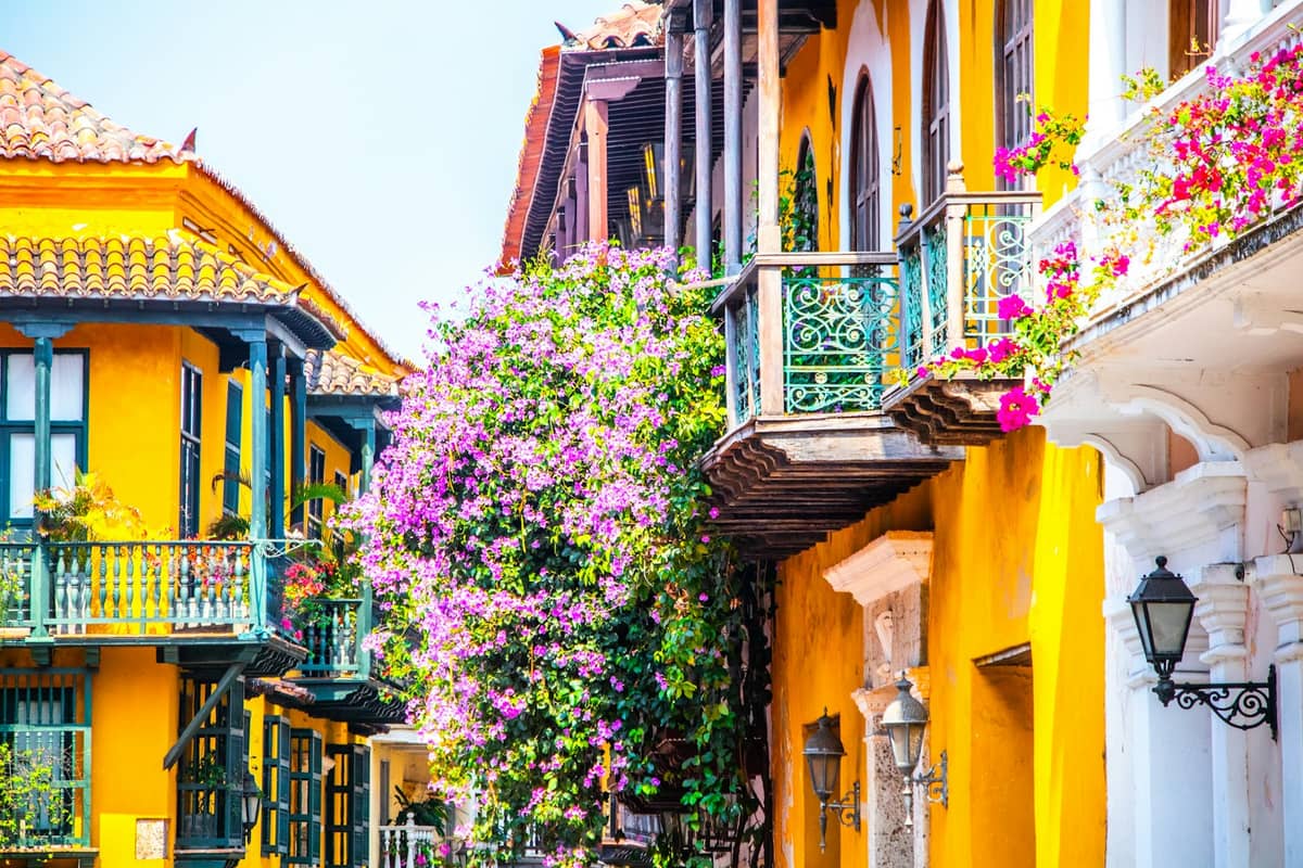 Brightly colored colonial buildings with wrought-iron balconies and bougainvillea flowers in Cartagena’s Walled City under sunny skies.
