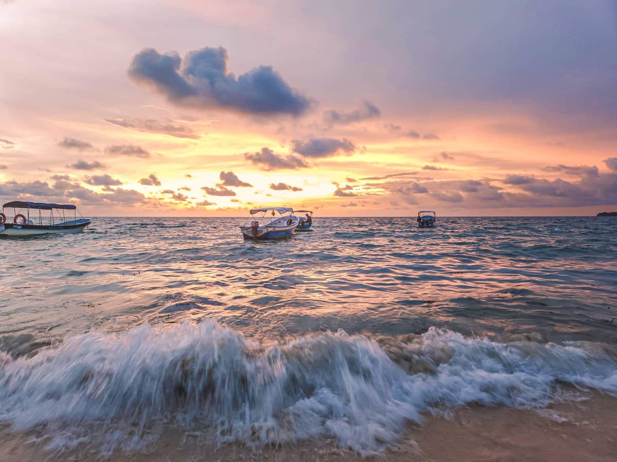 Small boats floating on turquoise water near a sandy beach at sunset, likely one of Cartagena’s Rosario Islands or Barú coastline.