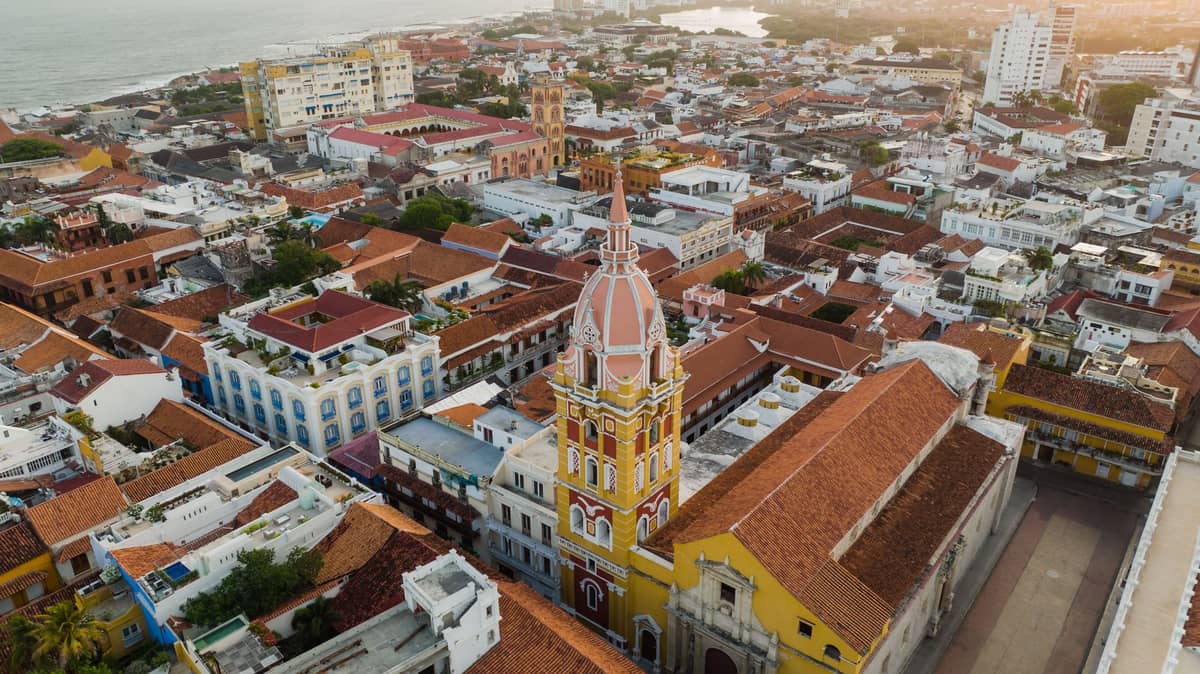 Aerial view of Cartagena's Walled City with the iconic cathedral tower, colonial rooftops, and courtyards, framed by the Caribbean sea at dusk.