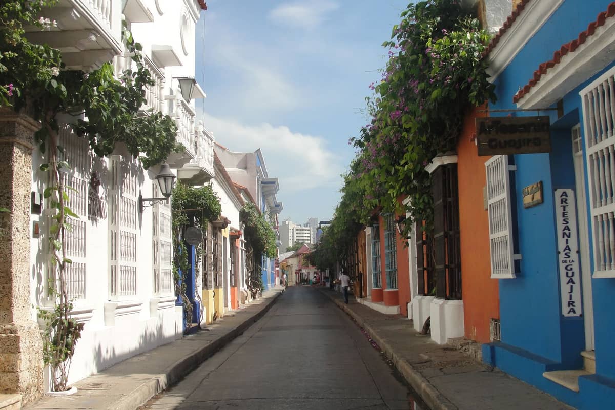 Colorful colonial street in Getsemaní, Cartagena, Colombia, with flowering vines, white and blue buildings, and a quiet urban atmosphere
