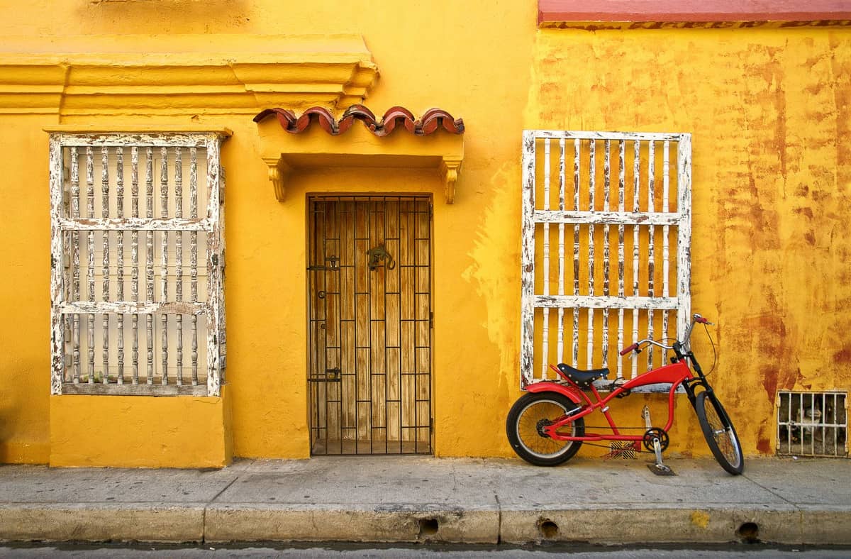 Yellow painted building with barred windows, central metal door, and a red bicycle parked outside on a Cartagena street.