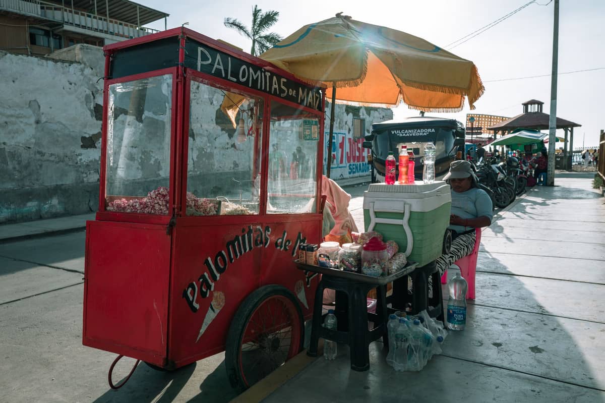 Street food cart labeled 'Palomitas de Maíz' with umbrella and snacks on Cartagena sidewalk in daylight.