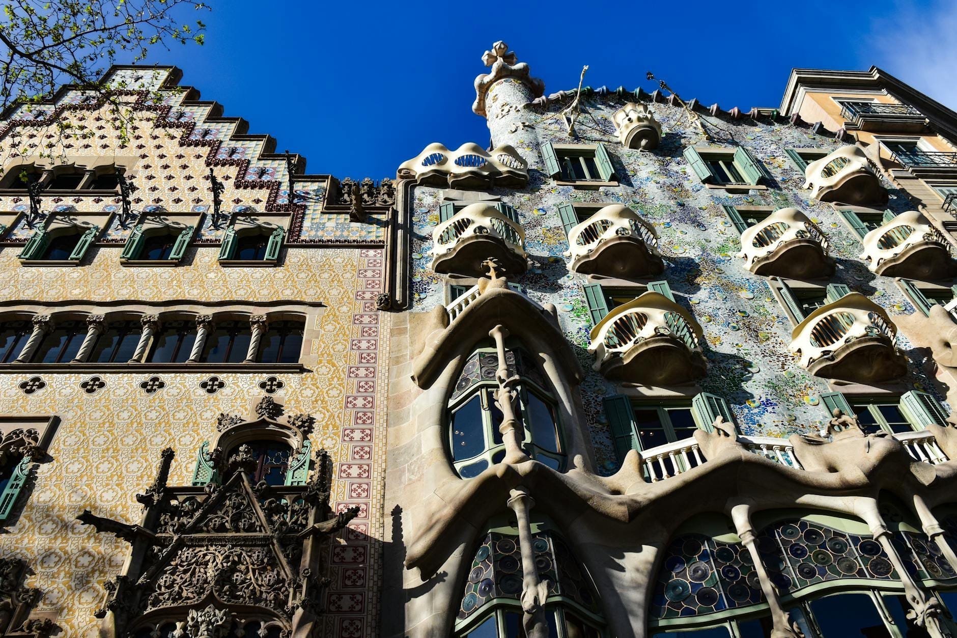 Colorful and ornate facade of Casa Batlló in Barcelona with bone-like balconies, iridescent ceramics, and sculptural rooftop seen under bright blue sky.